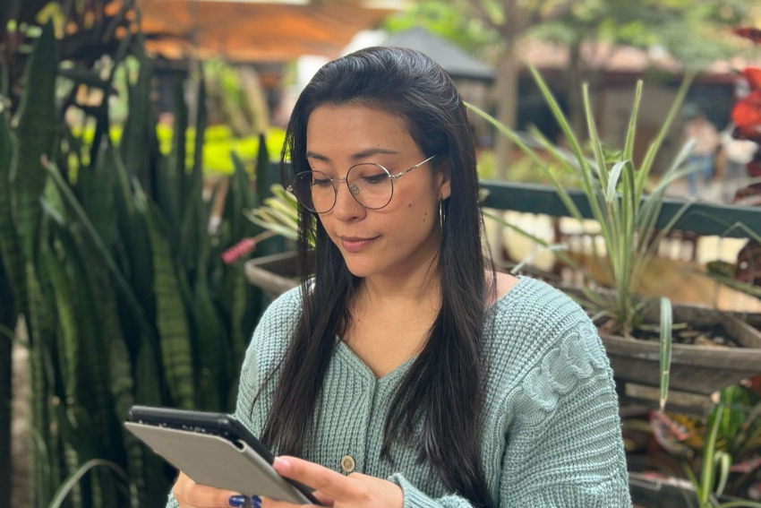 Persona con gafas y suéter verde menta leyendo en una tablet en un ambiente natural.