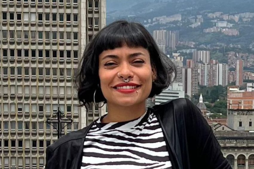 Ana Paulina, terapeuta aliada de El Diván Rojo, sonriente frente al paisaje urbano de Medellín, con corte de cabello corto y flequillo, vistiendo camiseta de rayas blancas y negras.