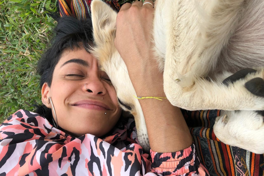 Ana Paulina, terapeuta aliada de El Diván Rojo, acostada en el césped, abrazando tiernamente a su perro, mostrando una expresión de paz y complicidad.